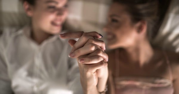 Close up of two smiling women relaxing together while holding hands. Focus is on foreground.